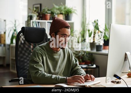 Jeune ingénieur INFORMATIQUE sérieux travaillant avec des informations codées tout en étant assis devant un moniteur d'ordinateur dans un bureau ouvert Banque D'Images