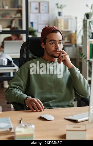 Jeune ingénieur INFORMATIQUE moderne assis sur le lieu de travail devant l'ordinateur et regardant l'écran tout en démarrant un nouveau programme de décodage des informations Banque D'Images