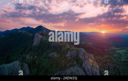 Silhouettes hautes d'épinette foncée sur les pentes des hautes montagnes de Rhodope sur fond de coucher de soleil ciel nuageux multicolore avec soleil. Panorama, vue de dessus Banque D'Images