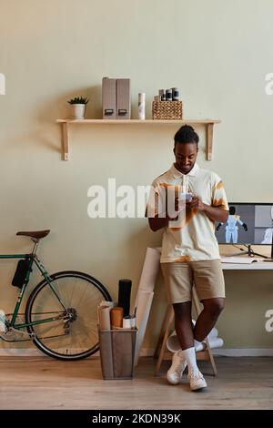 Portrait vertical du jeune homme noir comme concepteur numérique 3D utilisant un smartphone par lieu de travail Banque D'Images