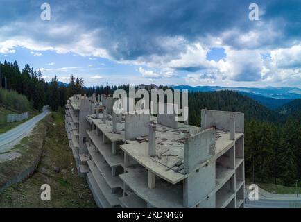 Ruines d'hôtel abandonné inachevé avec murs en béton et plusieurs étages dans la forêt d'épicéa sur le flanc de la montagne dans la vallée de Rhodope. Panorama, vue de dessus Banque D'Images