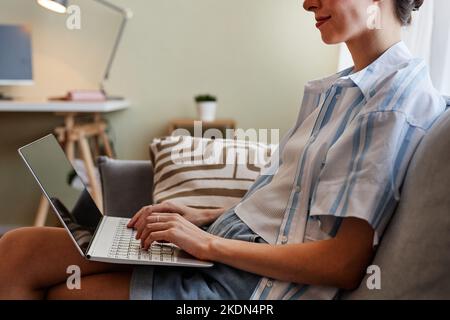Portrait court d'une jeune femme souriante utilisant un ordinateur portable tout en étant assise sur un canapé à la maison et au travail Banque D'Images