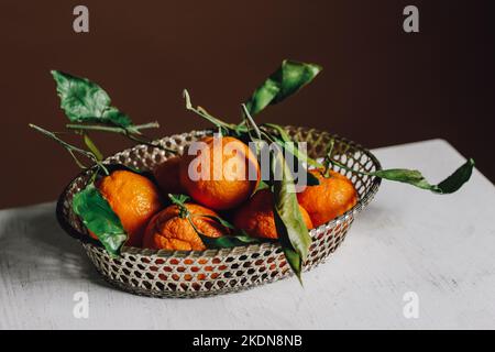 panier en métal rempli de fruits orange mandarin et de feuilles vertes Banque D'Images