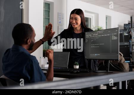 Des ingénieurs système heureux célèbrent la réussite de la compilation de scripts de code, en effectuant un geste de cinq mains après le développement du système. Équipe de développeurs Web analysant l'algorithme et créant une interface de serveur d'applications. Banque D'Images