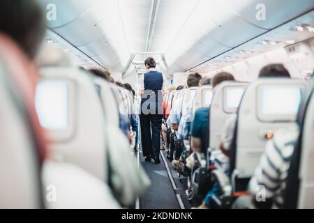 Intérieur de l'avion avec les passagers des sièges et hôtesse en uniforme autour de l'allée. Banque D'Images