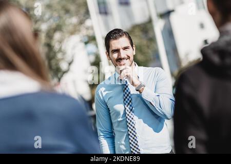 Beau jeune homme avec un sourire amical informel ayant hors du bureau réunion sur un suny jour. Banque D'Images