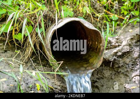 Eau s'écoulant de la sortie ouverte d'un carreau de drainage agricole métallique Banque D'Images