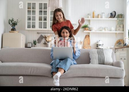 Joyeuse femme surjoyeuse assis sur le canapé tenant la boîte cadeau de l'adolescente debout derrière la mère Banque D'Images