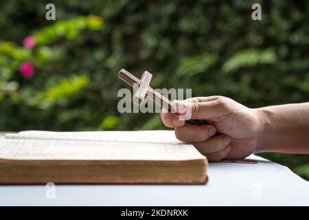 Homme tenant une croix religieuse en bois crucifix avec une Bible ouverte. Concept de foi chrétienne. Banque D'Images