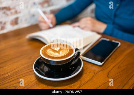 Femme lisant et écrivant sur un livre avec une tasse de café sur une table en bois Banque D'Images