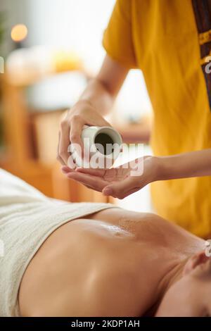 Mains de masseuse appliquant de l'huile de massage sur le dos de la femme Banque D'Images