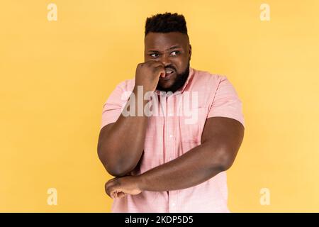 Trouble anxieux. Portrait de l'homme stressé hors inquiet dans le maillot rose mordant les ongles, nerveux au sujet des problèmes, paniquant et regardant peur, regardant loin. Studio d'intérieur isolé sur fond jaune. Banque D'Images