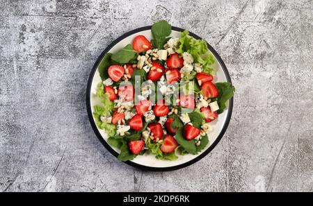 Salade de fromage bleu et d'arugula aux fraises avec pignons de pin sur une assiette ronde sur fond gris foncé. Vue de dessus, plan d'appartement Banque D'Images