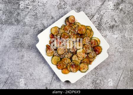 Sunomono - salade de concombres japonais aux graines de sésame sur une assiette carrée blanche sur fond sombre. Vue de dessus, plan d'appartement Banque D'Images