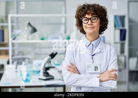 Jeune femme brunette réussie clinicien ou scientifique expert en laboure et lunettes croisant les bras par la poitrine et regardant la caméra Banque D'Images