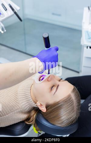 Les dents d'une femme avec des bretelles métalliques sont traitées à la clinique. Un orthodontiste utilise des instruments dentaires pour placer des bretelles sur les dents d'un patient. Sélection Banque D'Images