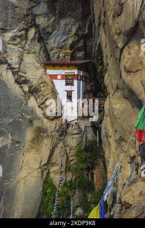 Superbe dépendance du monastère bouddhiste de Paro Taktsang alias Tiger's Nest construit entre des falaises rocheuses dans l'ouest du Bhoutan avec des drapeaux de prière traditionnels Banque D'Images