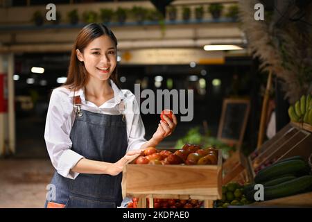 Portrait d'une femme asiatique propriétaire de la boîte de légumes en organisant les tomates sur les étagères du magasin. Concept de marché agricole Banque D'Images