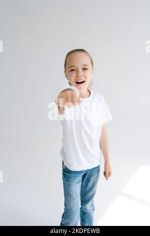 Portrait vertical de la petite fille courageuse souriante avec la main cassée enveloppée dans le bandage de plâtre blanc jouant des gestes avec le poignet blessé. Banque D'Images