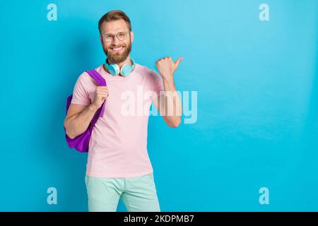Photo portrait de jeune homme attrayant casque hipster point vide espace porter des vêtements roses tendance isolés sur fond de couleur cyan Banque D'Images