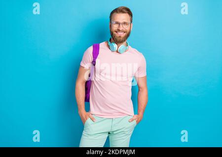 Photo portrait de beau jeune homme écouteurs hippster sac à dos étudiant porter des vêtements roses tendance isolés sur fond de couleur cyan Banque D'Images