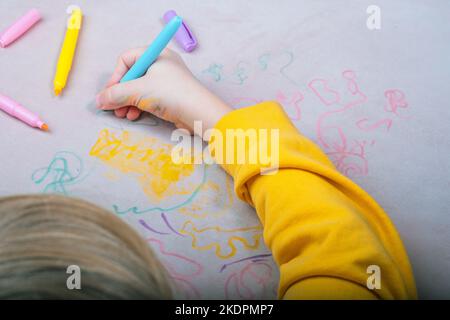 La main de l'enfant dessin avec un stylo feutre sur la sellerie du canapé. Vue du dessus. Tissus de mobilier. Concept de nettoyage Banque D'Images