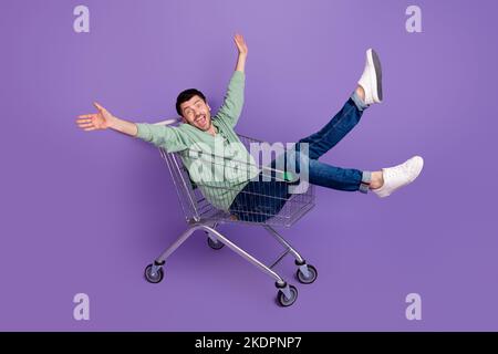 Portrait complet de l'homme positif surjoyé s'assoir chariot de marché isolé sur fond violet de couleur Banque D'Images