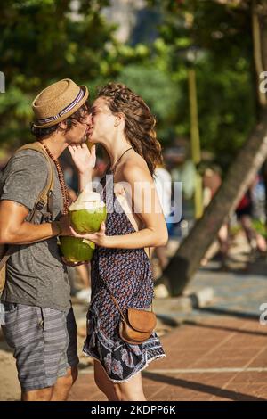 Des baisers tropicaux. Un jeune couple affectueux qui se détend sur la plage pour prendre un cocktail. Banque D'Images