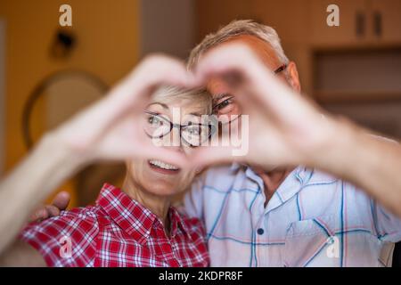 Un couple senior heureux s'embrasse et se forme le cœur avec ses mains. Banque D'Images