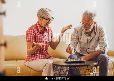 Couple senior assis dans la salle de séjour et jouant aux échecs. Activités de loisirs. Banque D'Images