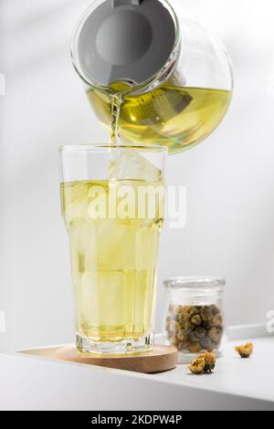 Verser le thé glacé au chrysanthème dans le verre de la table blanche Banque D'Images