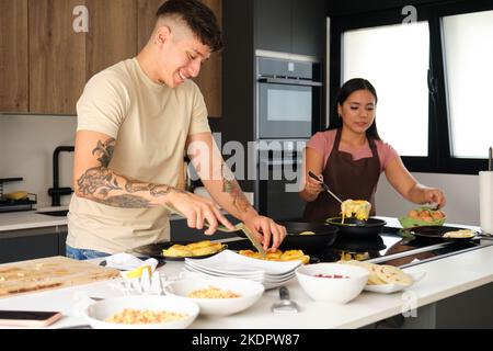 Deux jeunes latins cuisant des arepas traditionnels et des lapingachos. Banque D'Images