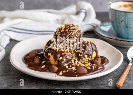 Dessert profiterole sur fond sombre. Cuisine française traditionnelle. Dessert à la profiterole recouvert de morceaux de chocolat et de noisettes. Gros plan Banque D'Images