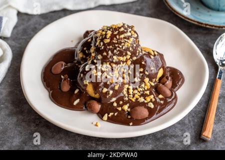 Dessert profiterole sur fond sombre. Cuisine française traditionnelle. Dessert à la profiterole recouvert de morceaux de chocolat et de noisettes. Gros plan Banque D'Images