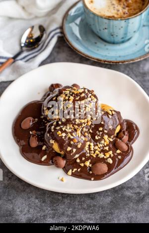 Dessert profiterole sur fond sombre. Cuisine française traditionnelle. Dessert à la profiterole recouvert de morceaux de chocolat et de noisettes. Gros plan Banque D'Images