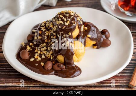 Dessert profiterole sur fond de bois. Cuisine française traditionnelle. Dessert à la profiterole recouvert de morceaux de chocolat et de noisettes. Gros plan Banque D'Images