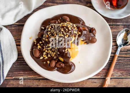 Dessert profiterole sur fond de bois. Cuisine française traditionnelle. Dessert à la profiterole recouvert de morceaux de chocolat et de noisettes. Gros plan Banque D'Images