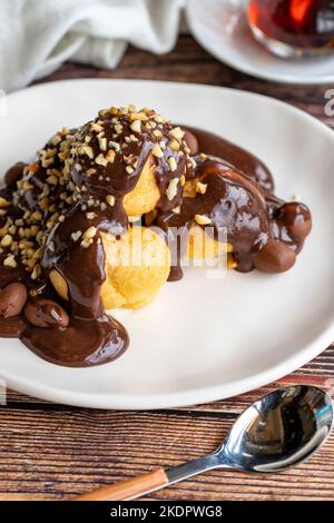 Dessert profiterole sur fond de bois. Cuisine française traditionnelle. Dessert à la profiterole recouvert de morceaux de chocolat et de noisettes. Gros plan Banque D'Images