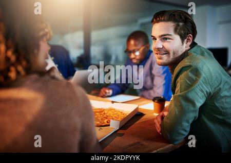 Une équipe de jeunes hommes d'affaires qui mangent de la pizza tout en travaillant tard au bureau. Banque D'Images