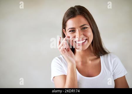 Une peau radieusement saine. Portrait d'une belle femme appliquant un hydratant à sa peau parfaite. Banque D'Images