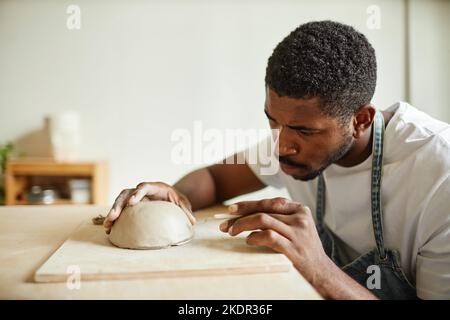 Portrait minimal d'un artiste masculin décorant un bol en céramique fait main dans un studio de poterie, espace de copie Banque D'Images