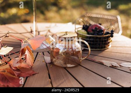 Pique-nique d'automne confortable dans le parc. Gros plan sur une bouilloire en verre avec thé noir chaud, tasses classiques, tarte aux pommes maison, feuilles d'érable et bougies sur le woo Banque D'Images