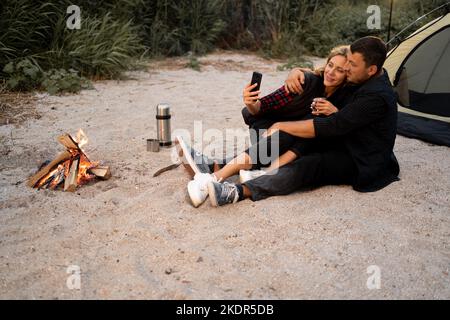 Camping couple dans une tente prenant un selfie. Couple heureux faisant selfie tout en étant assis au camping. Les gens, le style de vie et la technologie Banque D'Images