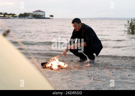 tourisme autour du feu de camp le soir sur le rivage de la rivière. camping sur le rivage du lac. homme reposant près du feu de camp et de la tente. Tourisme et mode de vie actif Banque D'Images