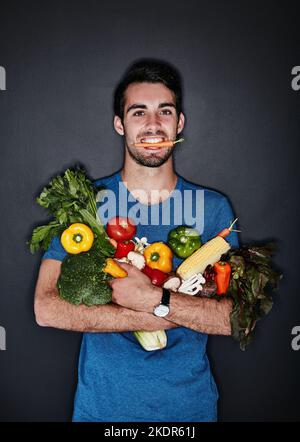 IVE a fait le bon choix. Portrait en studio d'un jeune homme portant une quantité de légumes sains sur un fond sombre. Banque D'Images