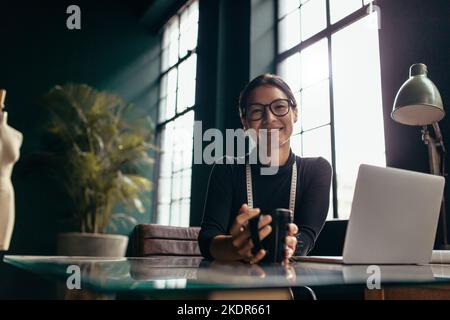 Portrait d'une styliste souriante assise à son bureau. Femme créative assise au bureau avec café. Banque D'Images