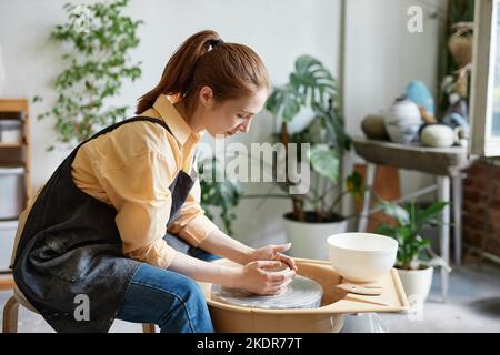 Portrait de la jeune femme en train d'utiliser la roue de poterie et de créer des céramiques faites à la main dans un studio confortable Banque D'Images