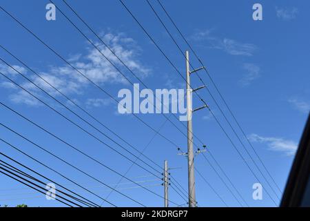 Poteaux électriques et lignes électriques aériennes placés contre un ciel bleu lumineux avec des nuages blancs. Banque D'Images