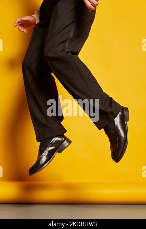 Image courte des jambes de sexe masculin dans un pantalon et des bottes noirs sautant sur fond jaune de studio Banque D'Images