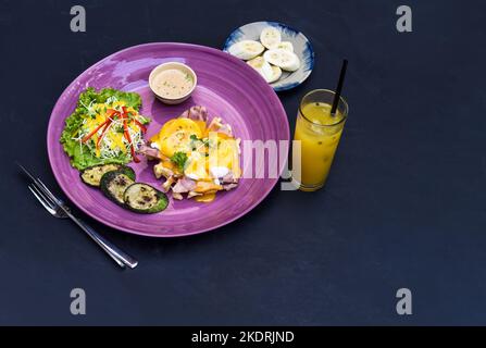 Œufs Benedict (œufs pochés) sur jambon grillé avec sauce hollande sur gaufres belges avec courgettes grillées avec assiette de banane et une tasse de jus de passion Banque D'Images